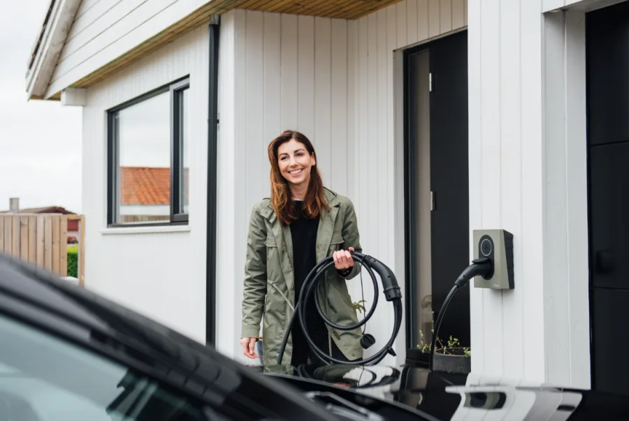 Kvinne lader elbil med ladekabel fra veggmontert ladeboks